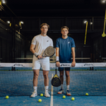 Two athletes wearing the Performance Shirt Navy, posing on the padel court with rackets, demonstrating the shirt’s comfort, style, and suitability for active play.